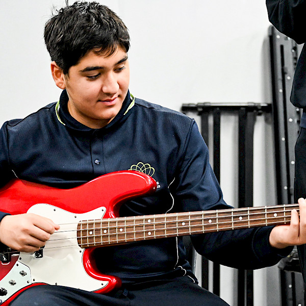 Student playing a red electric bass guitar in an Instrumental Music lesson