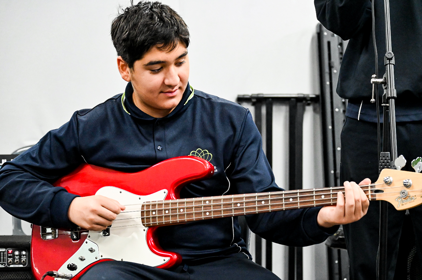 Student playing a red electric bass guitar in an Instrumental Music lesson