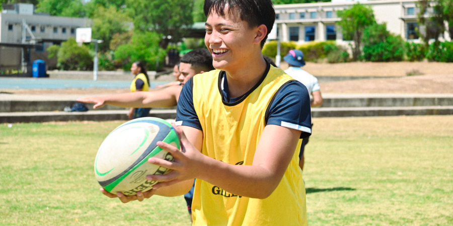 Rugby Academy student in a yellow training bib passing a rugby ball on the college oval